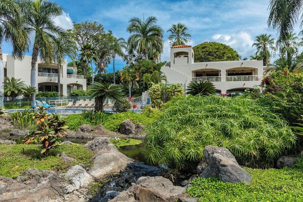 A resort with a pool, palm trees, and a small stream.