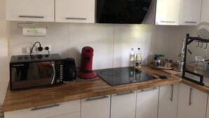Una cocina moderna con armarios blancos, una cocina por inducción negra, un hervidor rojo y una cafetera.