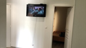 Un dormitorio con una cama, un televisor montado en la pared y una puerta que da a otra habitación.
