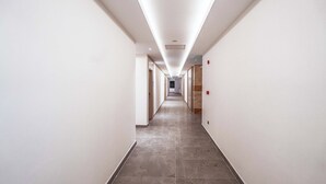 A long, narrow hallway with white walls and a tiled floor, leading to a door at the end.