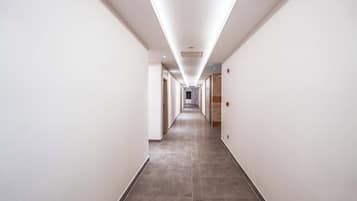 A long, narrow hallway with white walls and a tiled floor, leading to a door at the end.