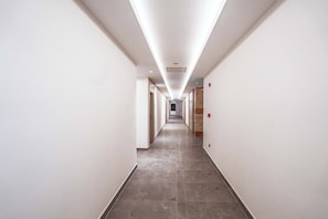 A long, narrow hallway with white walls and a tiled floor, leading to a door at the end.