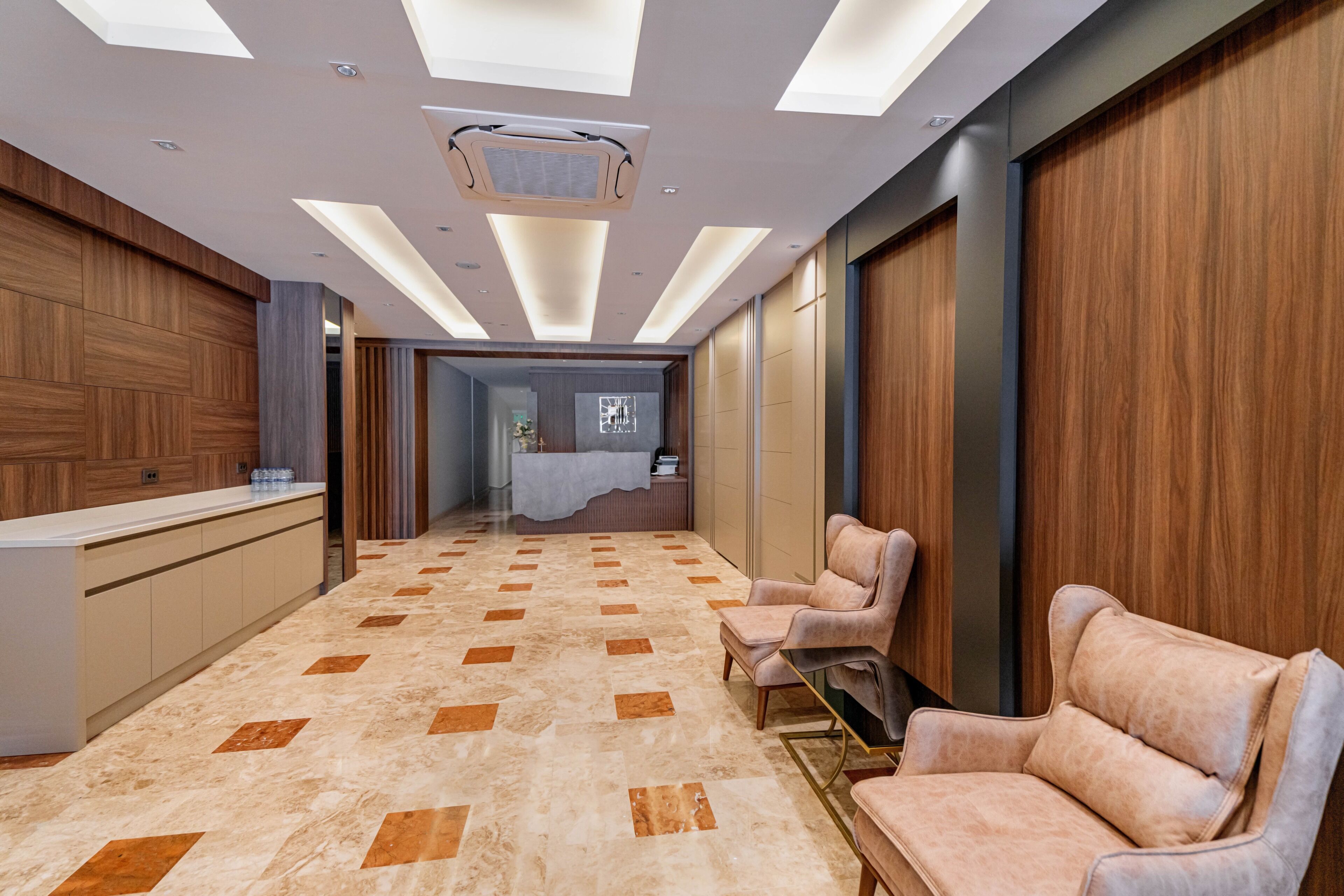 A modern hotel lobby with a reception desk, seating area, and a view into a bedroom.