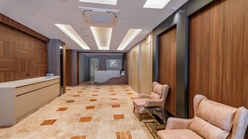 A modern hotel lobby with a reception desk, seating area, and a view into a bedroom.