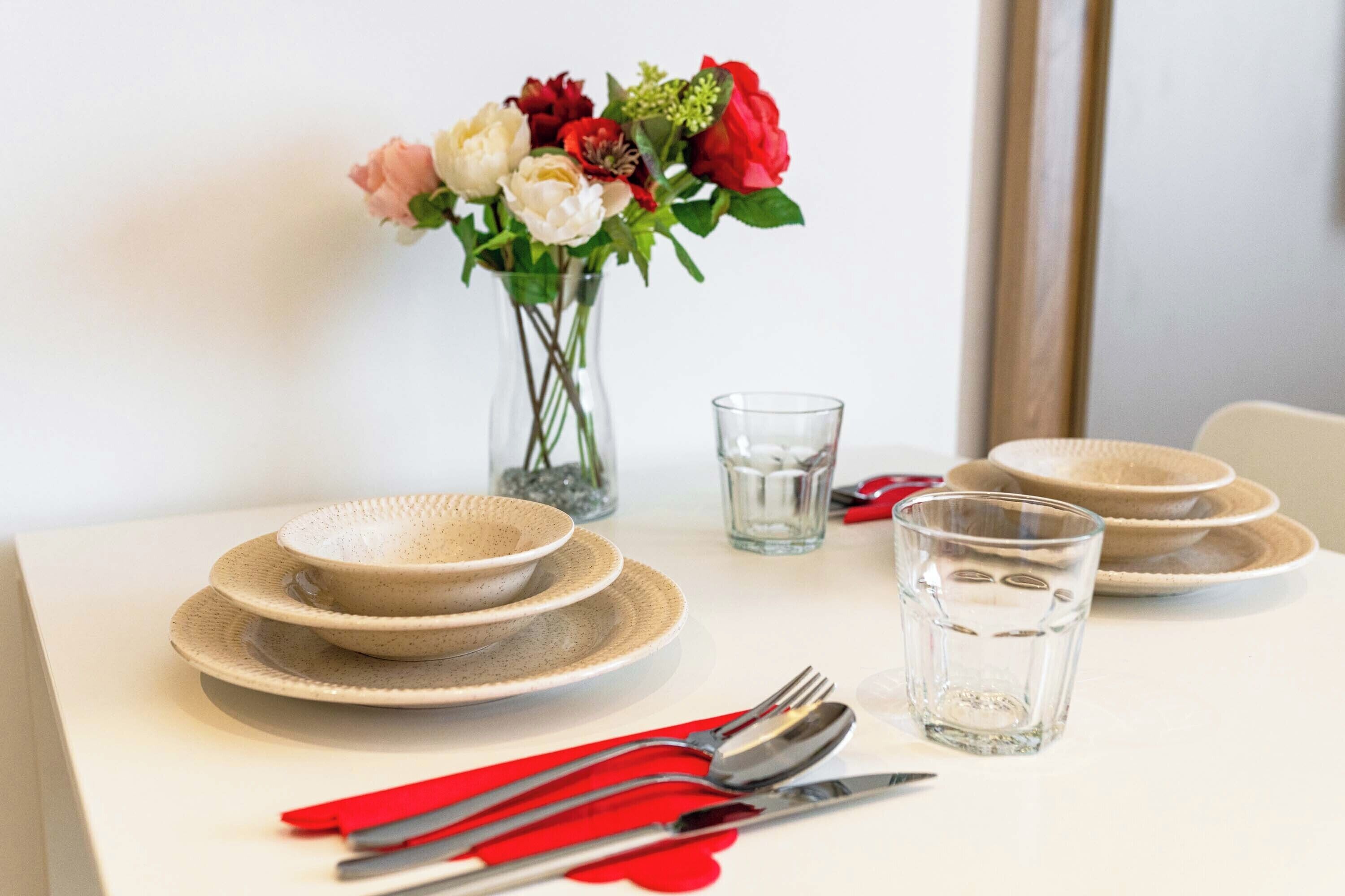 Una mesa de comedor con platos, cubiertos, una copa y un florero con flores.