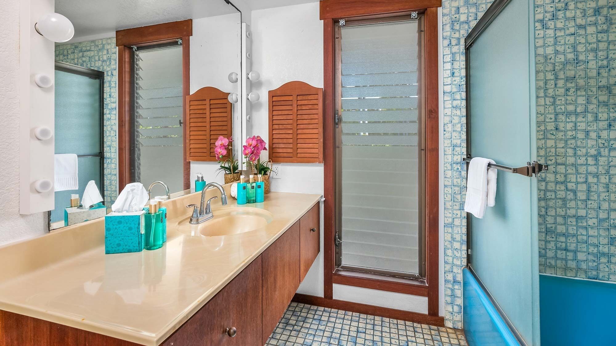 A bathroom with a beige sink, wooden cabinets, a large mirror, and a shower with frosted glass doors.