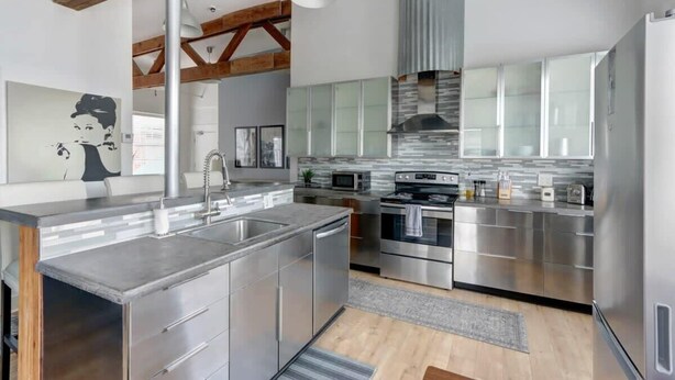 Een moderne keuken met roestvrijstalen apparatuur, een centraal eiland en een hoge plafond met zichtbare balken.