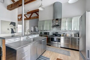 Una cocina moderna con electrodomésticos de acero inoxidable, una isla central y un techo alto con vigas a la vista.