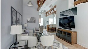 Een moderne woonkamer met een televisie, witte meubels en een houten plafondconstructie.
