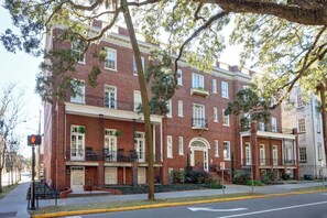 A two-story brick building with a central entrance, windows on each floor, and a small balcony on the second floor.
