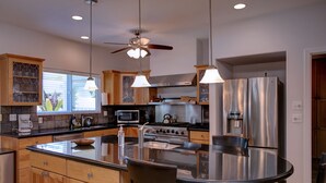 A modern kitchen with wooden cabinets, stainless steel appliances, and a central island with seating. - Hawaiian Dream with Pool (Pepeekeo)