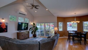 A spacious living room with a large gray sectional sofa, a flat-screen TV, a ceiling fan, and a dining area with a table and chairs. - Hawaiian Dream with Pool (Pepeekeo)