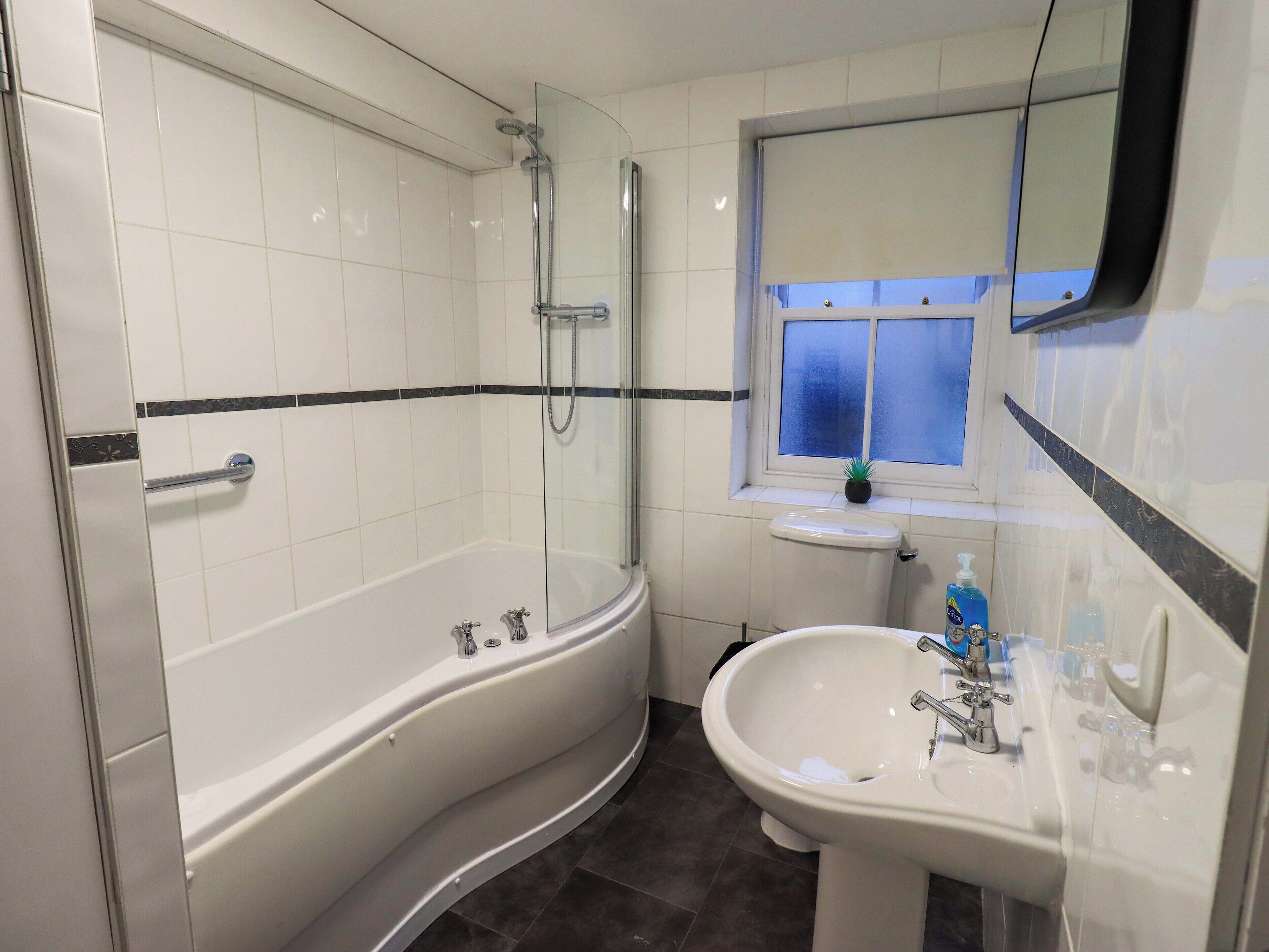 A modern bathroom with a glass-enclosed shower, a freestanding bathtub, a sink, and a window with a view.
