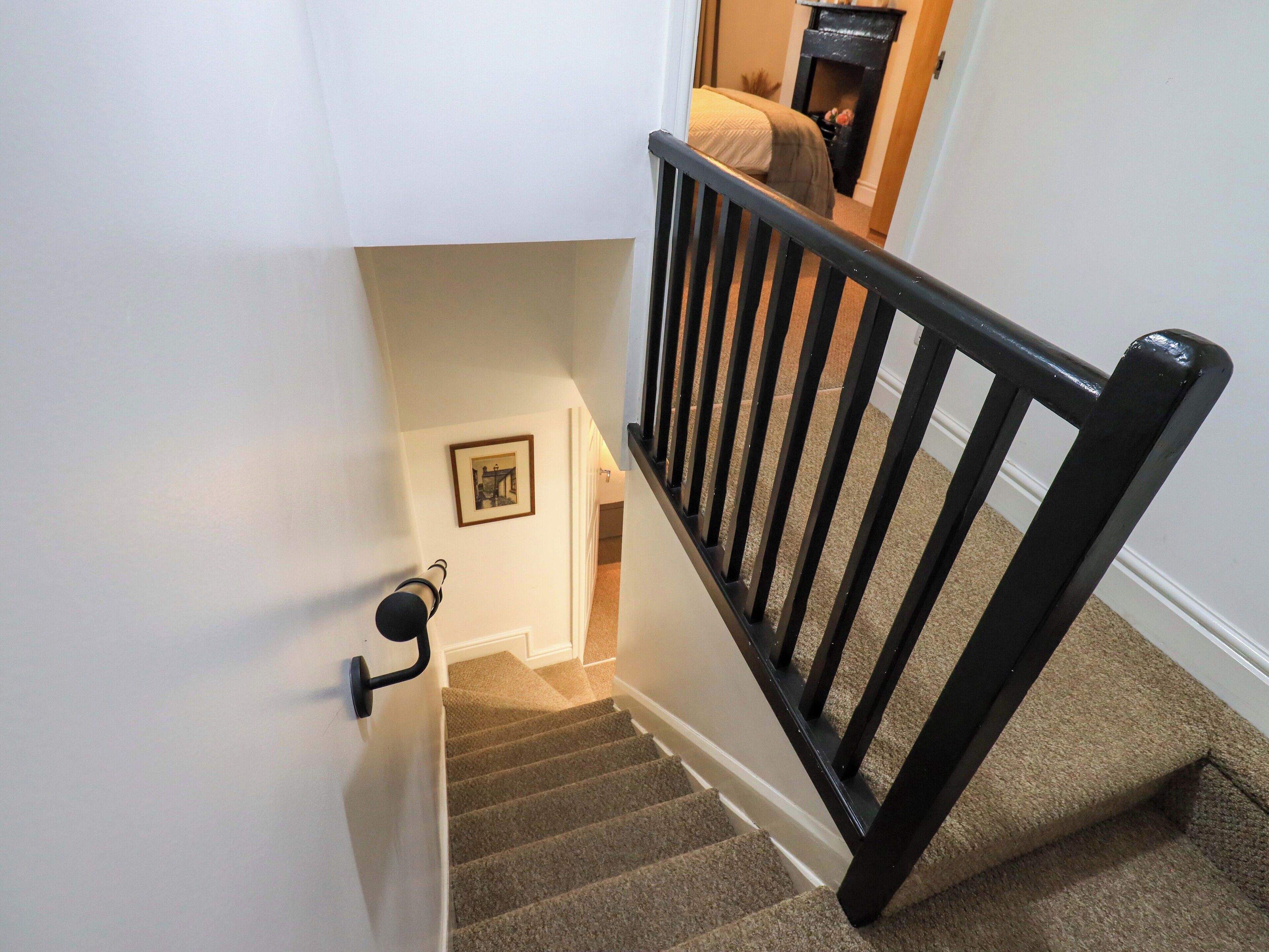 A carpeted staircase with a black handrail and a picture frame on the wall.