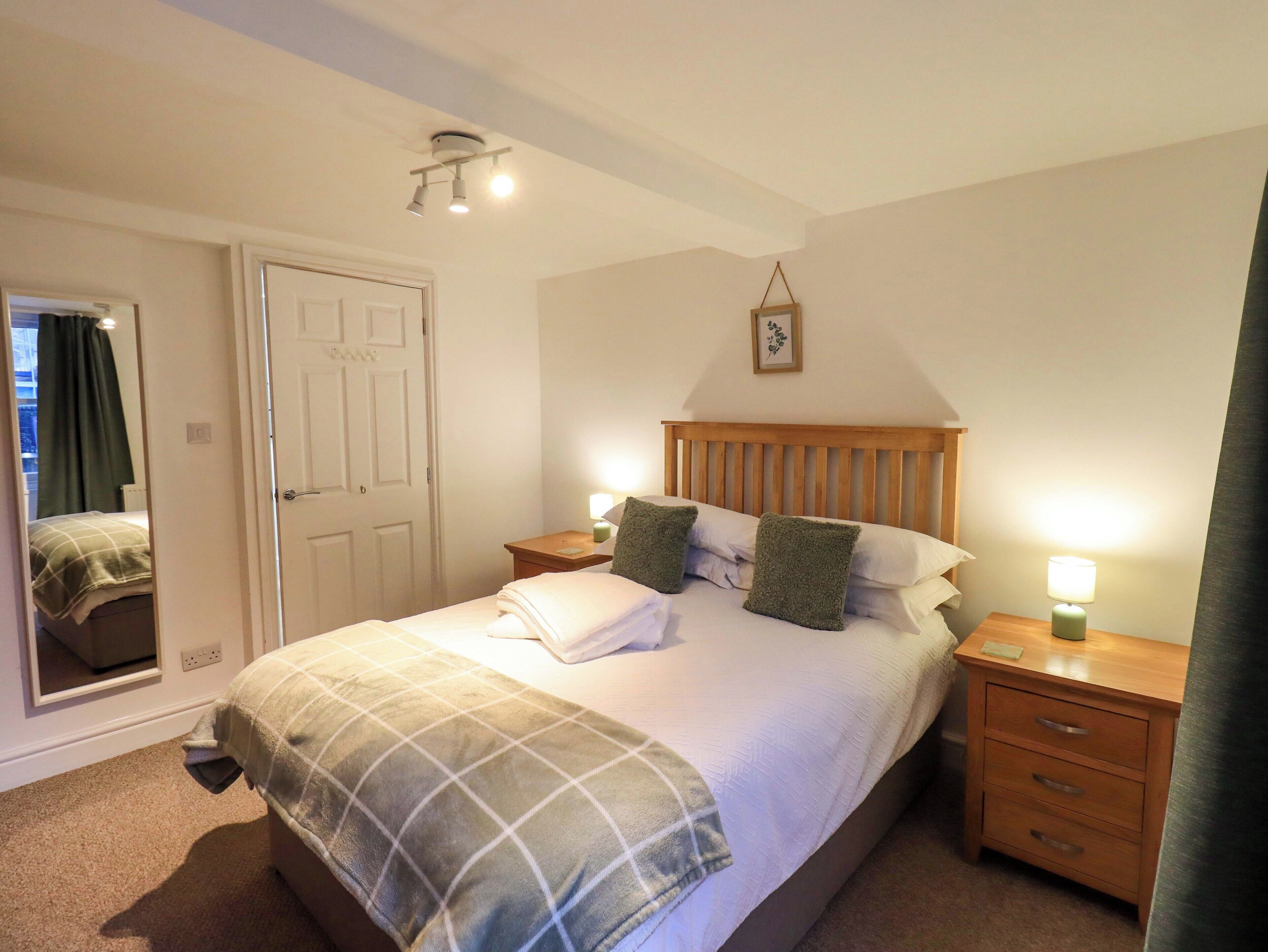 A neatly made bed with a plaid blanket, two bedside lamps, and a wooden headboard.
