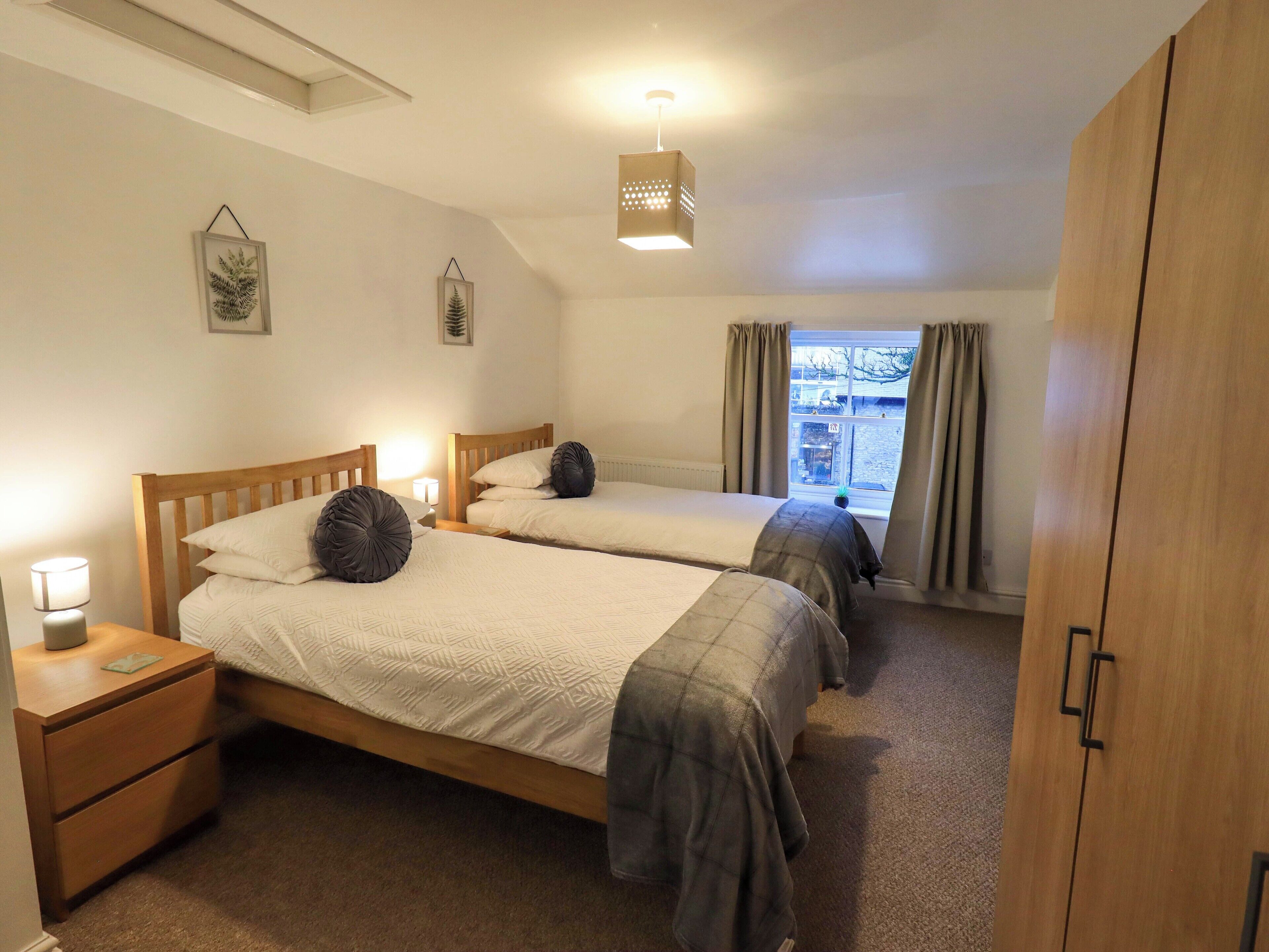A bedroom with two beds, a wooden wardrobe, and a window with curtains.