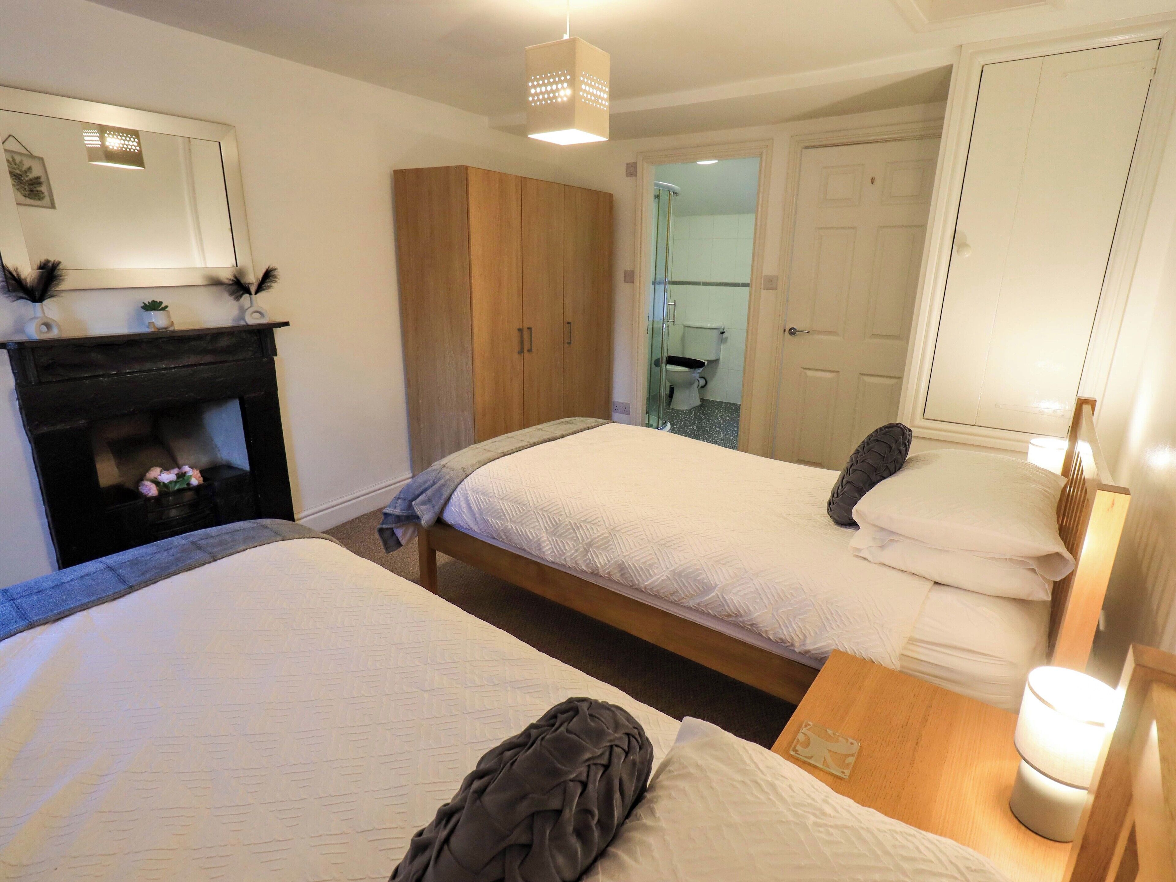 Une chambre d’hôtel avec deux lits, une armoire en bois, un miroir et une cheminée.