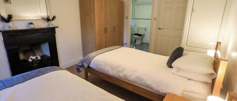 A hotel room with two beds, a wooden wardrobe, a mirror, and a fireplace.