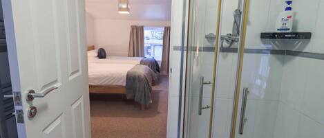 A hotel room with a shower, a bed with two pillows, and a window with curtains.
