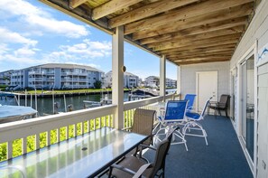 Un espace extérieur abrité, doté d’une table et de chaises en verre, qui offre une vue sur une marina avec des bateaux et des bâtiments en arrière-plan.