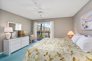 Une chambre d’hôtel comprenant un lit, une commode, une télévision, un ventilateur de plafond et un balcon avec vue sur les bâtiments.