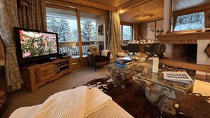 Un interior acogedor de cabaña con televisor, chimenea, comedor y ventanas amplias.