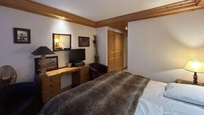 Un dormitorio con cama, escritorio, silla, televisor y armario.