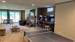 A living room with a ping pong table, gaming consoles, a fireplace, and a dining area with chairs and a table. - Family Friendly Mountain Townhouse in N. Woodstock (Woodstock)