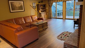 A living room with a leather sofa, wooden coffee table, and a rug. There is a staircase leading to a balcony with a view of the outside. - Family Friendly Mountain Townhouse in N. Woodstock (Woodstock)