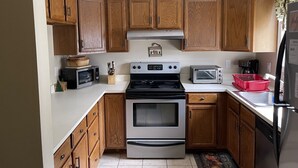 A compact kitchen with wooden cabinets, a stove, a microwave, a toaster, and a refrigerator. - Family Friendly Mountain Townhouse in N. Woodstock (Woodstock)