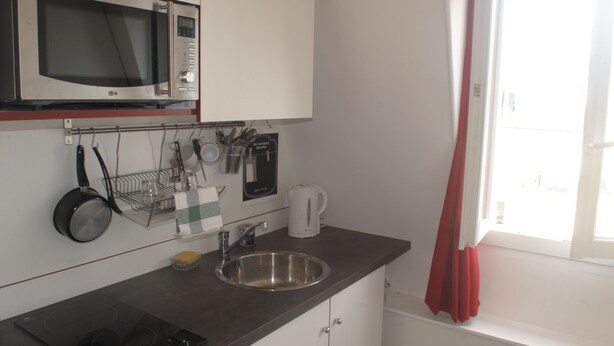 Een keuken met een magnetron, spoelbak en raam met gordijnen.