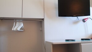 Een kamer met een wandtelevisie, een bureau met een lamp en een kledingrek.