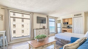 Une chambre avec un lit, une télévision, un bureau, une plante et une vue sur la mer.