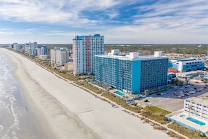 A beachfront hotel with multiple high-rise buildings, a swimming pool, and a parking area.
