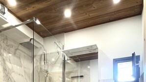 Un baño moderno con ducha envuelta en vidrio, tocador de madera con lavamanos, espejo y lavadora de carga frontal.
