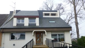 Une maison à deux étages avec une entrée à l’avant, un escalier et une voiture garée devant.