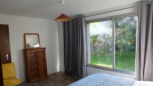Une chambre à coucher comprenant un lit, une armoire en bois, un miroir, un luminaire suspendu et une fenêtre avec des rideaux.