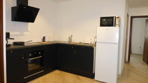Une cuisine de taille réduite avec des meubles noirs, un réfrigérateur blanc, un four à micro-ondes et une cuisinière.