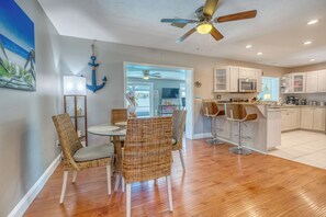A dining area with wicker chairs and a table, a kitchen with white cabinets and a microwave, and a ceiling fan.