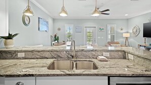 A kitchen with granite countertops, stainless steel sinks, pendant lighting, and a ceiling fan. - Destin Family Beach Townhouse (Destin)