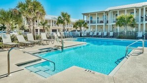 A swimming pool with lounge chairs and palm trees, surrounded by a building with balconies. - Destin Family Beach Townhouse (Destin)