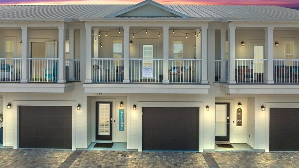 A two-story building with a balcony on the upper floor, a garage door on the ground floor, and a welcome sign. - Destin Family Beach Townhouse (Destin)