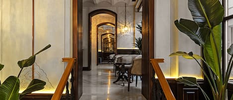 Un magnifique escalier en marbre, agrémenté de balustrades ouvragées, mène à une salle à manger bien éclairée, où se trouvent des tables et des chaises.