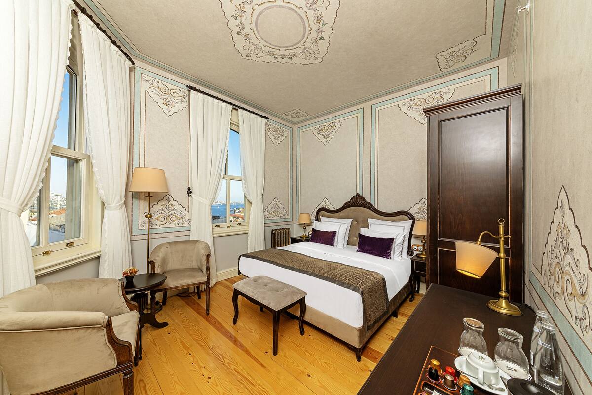 A hotel room with a large bed, two armchairs, a small table, and a desk with a lamp.