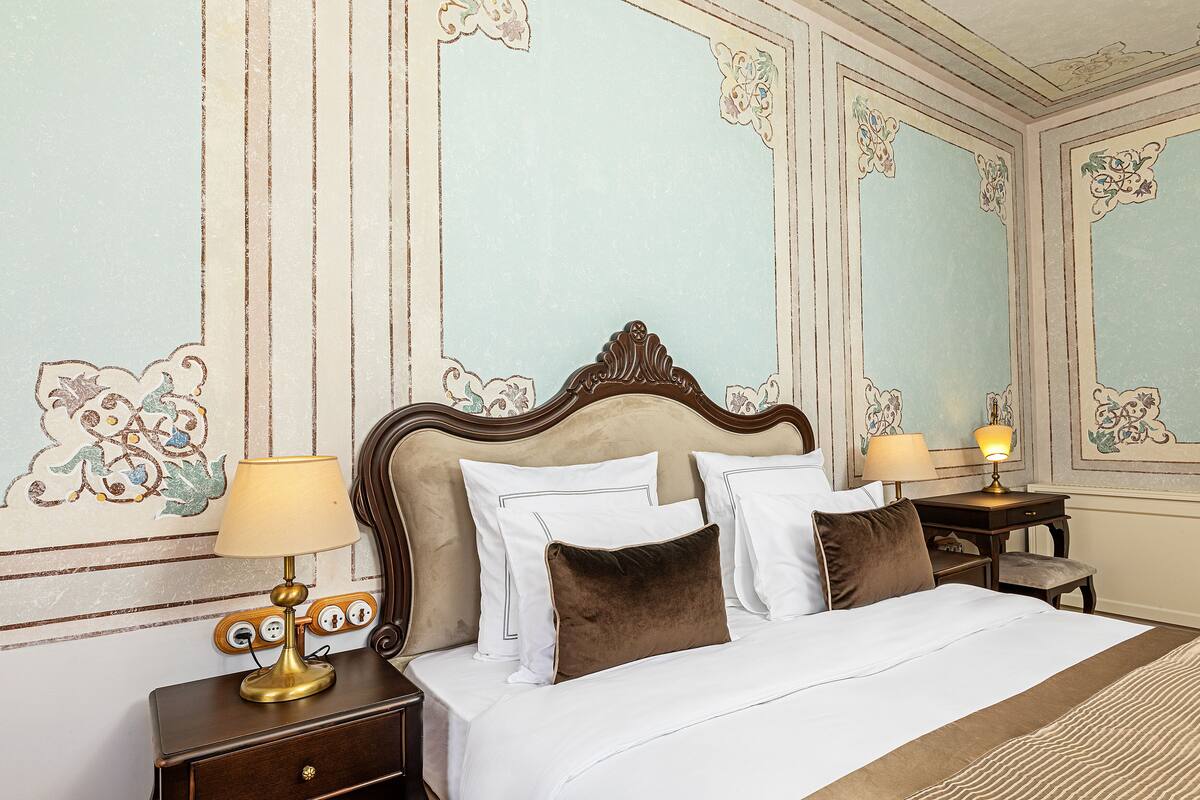 A neatly made bed with white linens and brown pillows, a bedside table with a lamp, and a wall with decorative paneling.
