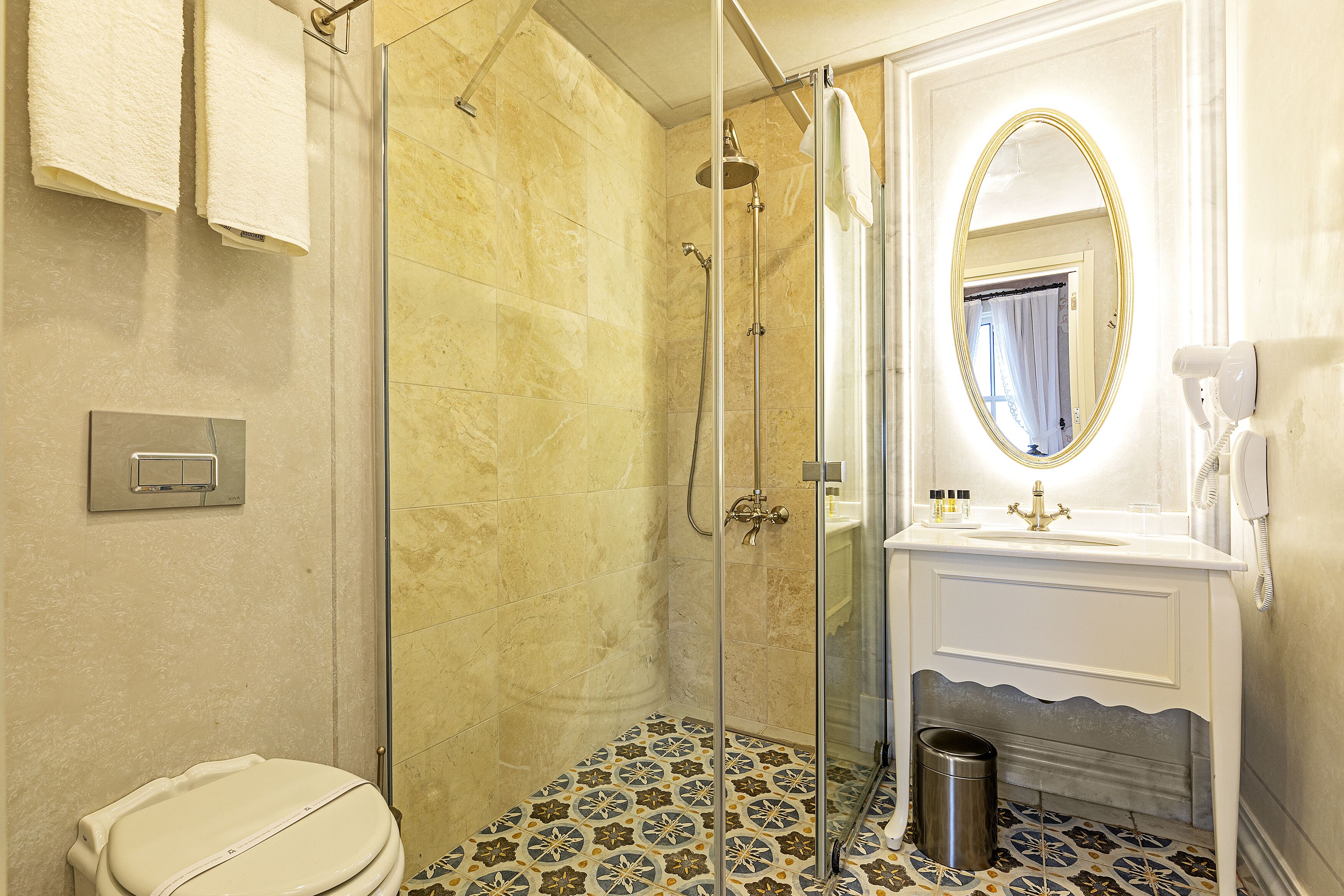 Un baño con ducha envuelta en vidrio, un lavabo blanco con espejo y baldosas de suelo con diseño.