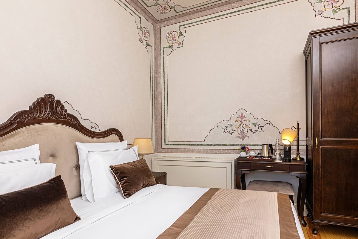 A neatly made bed with white and brown bedding, a wooden headboard, a bedside table with a lamp, and a wardrobe.
