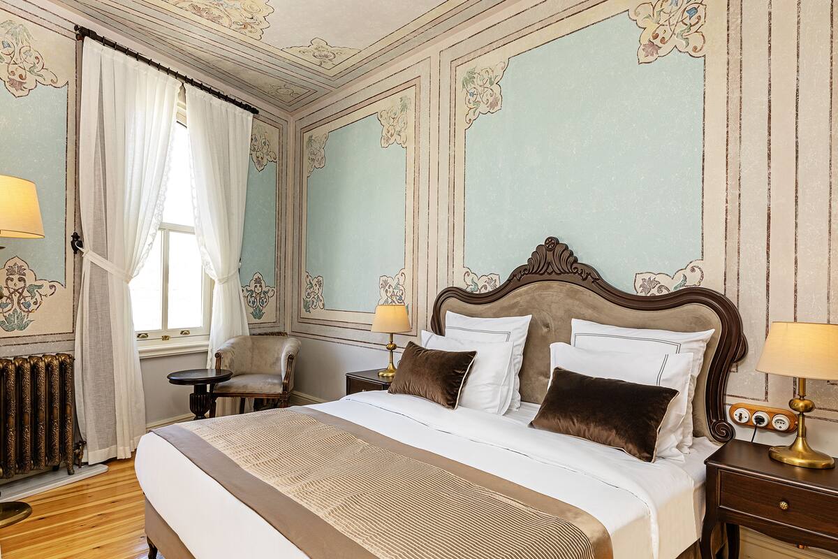 A classic hotel room with a large bed, two bedside tables with lamps, a chair, and a radiator.