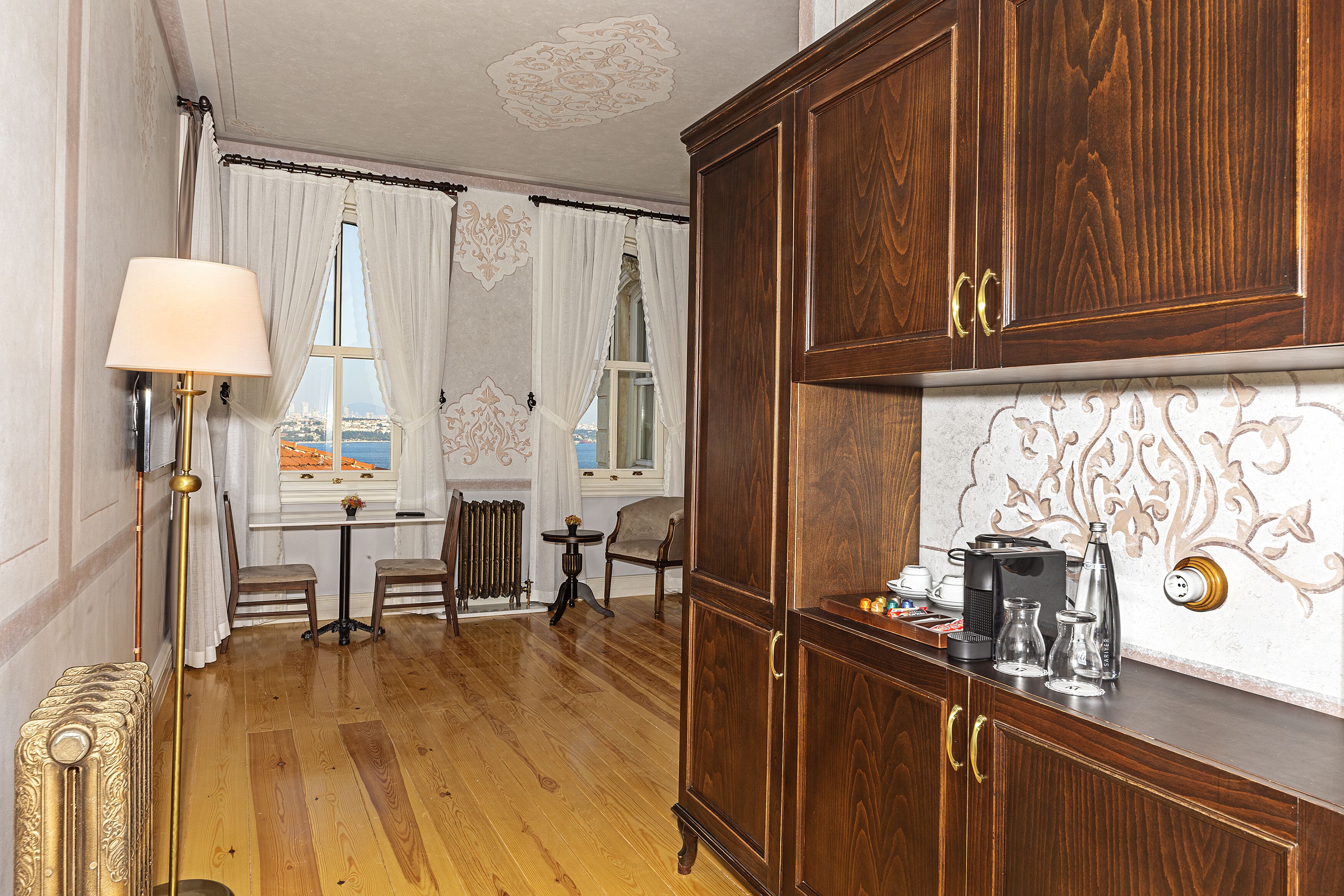 A room with a wooden cabinet, a radiator, a table with chairs, and a lamp.