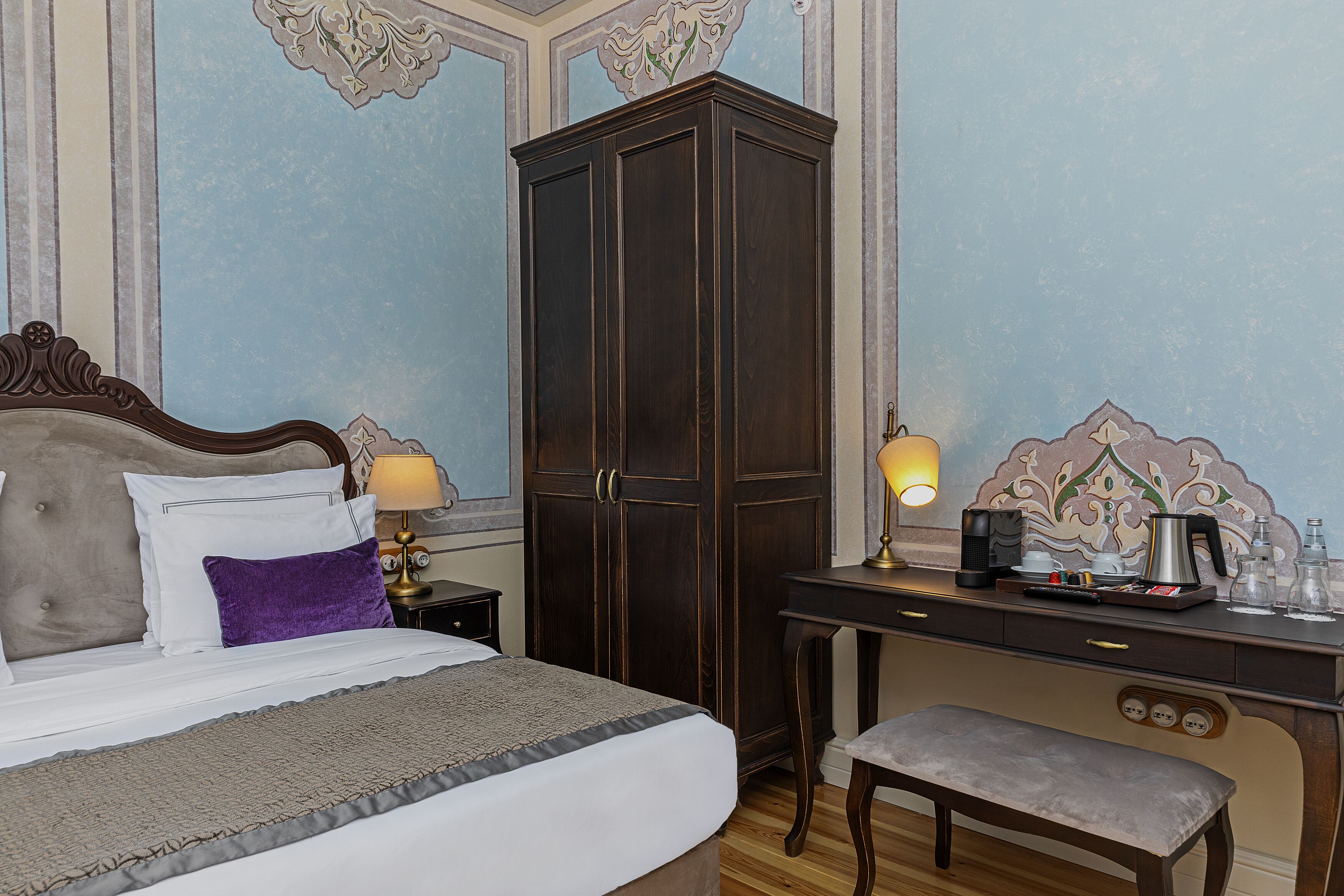 A hotel room with a bed, a desk, a cabinet, and a bench.